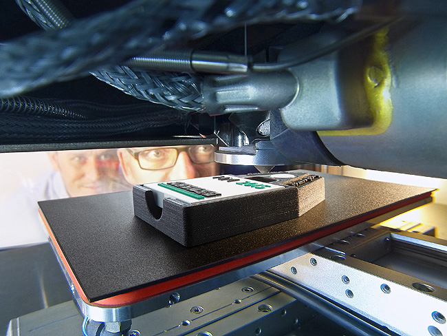 Freeformer construction chamber: The rocker-type light switch is placed in a holding device where an individualised symbol/name combination is applied in an additive process. The holding device itself was also made using the Arburg Plastic Freeforming (AKF) process